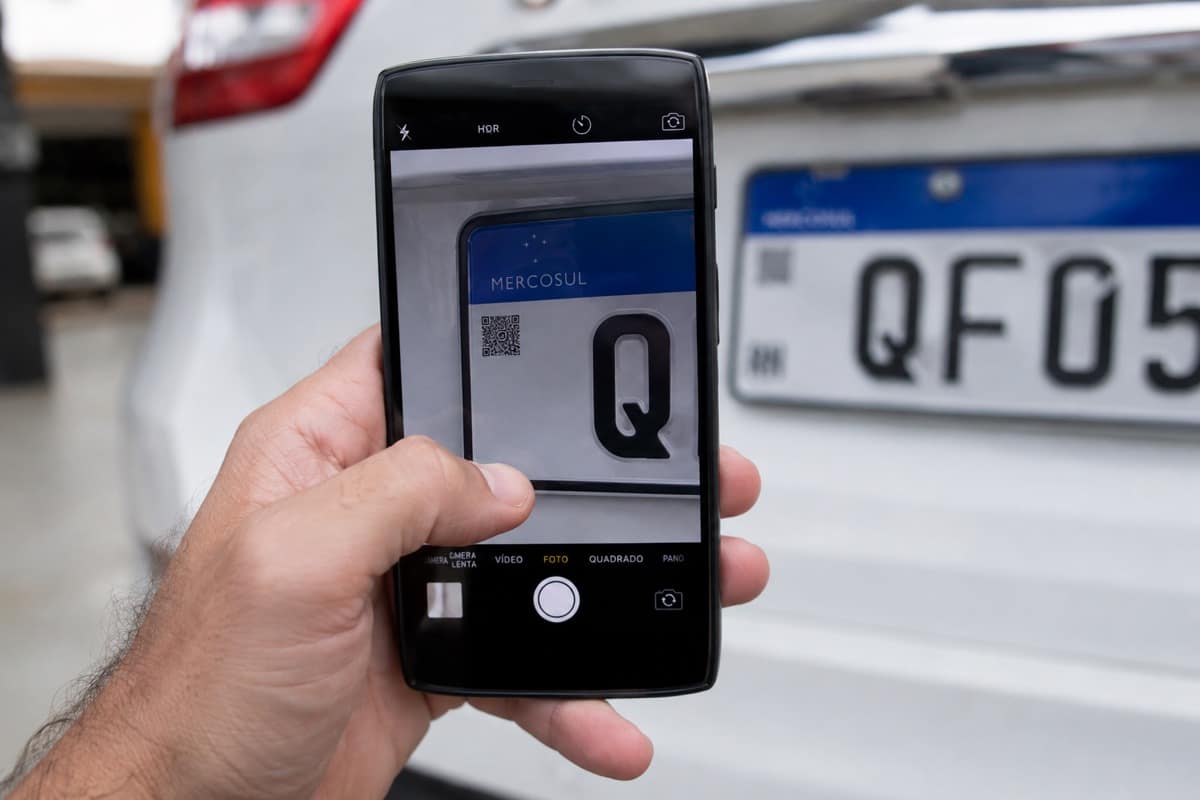 Mão segurando celular para ler o QR Code de uma placa Mercosul