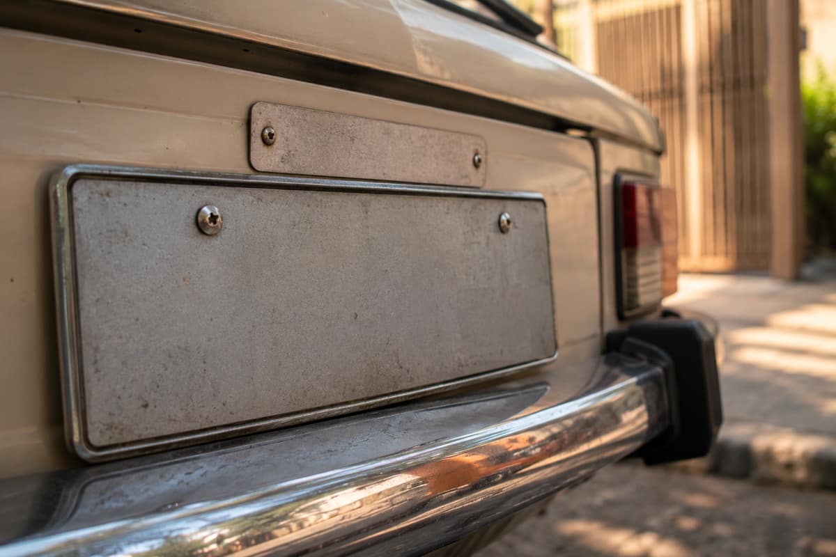 Traseira de carro antigo com placa cinza metálica e tarjeta parafusada acima dela