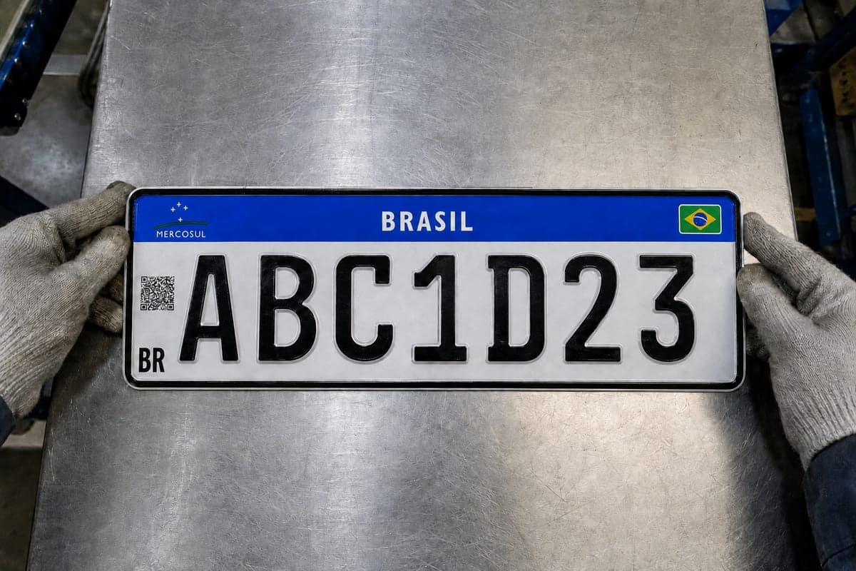 Mãos de um operador com luva apoiando uma placa recém-estampada na bancada da fábrica