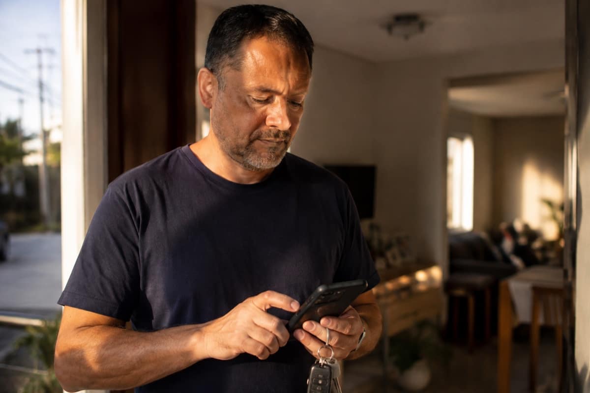 Homem digitando mensagem no celular com as chaves do carro na mão antes de sair de casa