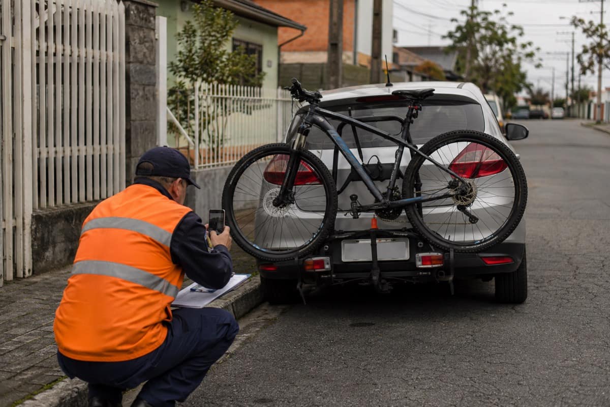 Fiscal de trânsito verificando bicicleta que cobre a placa traseira de um carro estacionado